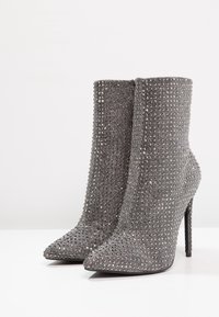 Bottines grises scintillantes en tissu texturé, recouvertes de strass. Elles présentent un bout pointu et un talon stiletto haut.
