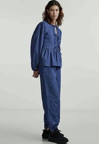 Μπλε ριγέ σετ δύο τεμαχίων που περιλαμβάνει τοπ με πιέτα και άνοιγμα στον λαιμό και ταιριαστά παντελόνια με χαλαρή εφαρμογή. Φοριέται με μαύρα αθλητικά παπούτσια.