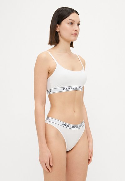 Balts kokvilnas bralette un saderīgs thong ar melnu logo jostu. Dizains ietver plānas siksnas un gludu, neizrotātu tekstūru.