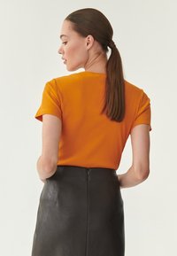 Oranžový žebrovaný top s krátkým rukávem, zkombinovaný s černou koženou sukní s hladkou texturou a zadním zipem.