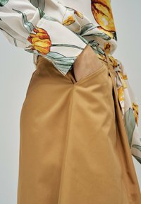 Falda beige con un bolsillo lateral, combinada con una blusa floral con estampado de tulipanes amarillos y hojas verdes. Textura de tela suave, ajuste entallado.