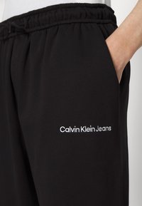 Μαύρες φόρμες από μαλακό ύφασμα, με ελαστική μέση και λευκό κεντητό λογότυπο "Calvin Klein Jeans" στο πλάι.