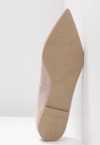 Lichtroze suède balletflat met een spitse neus, een textuurlijk zool met graphics van balletslippers en branding aan de onderkant.