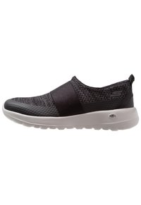 Chaussures noires à enfiler avec un dessus en tricot texturé, un bout en synthétique lisse et une semelle blanche rembourrée. Comprend un logo signature sur le côté.