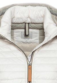 Lichte, crèmekleurige pufferjack met horizontaal gestikte patroon, een ritssluiting aan de voorkant en een label voor gerecycled materiaal. Gestreepte binnenkraag.