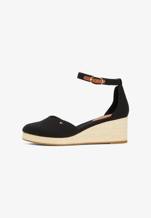 Zapato de cuña negro con plataforma beige tejida, punta cerrada, correa en el tobillo con hebilla dorada y pequeño logo rojo, blanco y azul en el lateral.