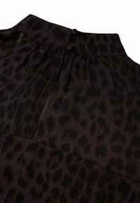 Blusa de animal print en púrpura oscuro y negro, con escote redondo, dos botones en la parte de atrás y una tela suave y transparente con una textura lisa.
