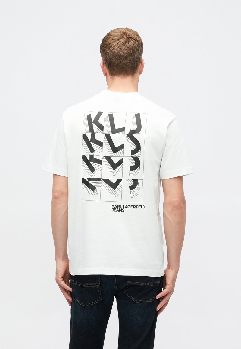 T-shirt branca de algodão com um design gráfico preto nas costas, apresentando letras e padrões geométricos. Gola redonda, mangas curtas, corte descontraído.