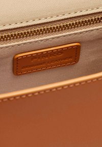 Bruine echte leren interieur met ritscompartiment, voorzien van een beige stoffen voering en een zichtbaar label "PINKO GENUINE LEATHER." Gouden rits.