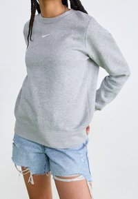 Grå sweatshirt med rund hals, Nike-logotyp i vitt, ribbade muddar och nederkant, tillsammans med slitna denimshorts. Materialet verkar mjukt och foder av fleece.
