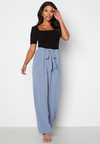 Sort ribbet top med firkantet udskæring og korte ærmer, kombineret med lyseblå højtaljede vidde bukser og beige vævede sandaler.