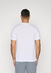 Hvit bomulls T-skjorte med korte ermer, rund hals, og et enkelt design. Båret med grå shorts, som viser en minimalistisk stil.