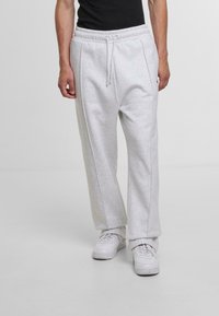 Light gray sweatpants with an elastic waistband, drawstring, and side seams, paired with white sneakers on a plain background.