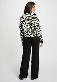 Pullover a stampa animale in bianco e nero con orlo e polsini a costine, indossato con pantaloni neri morbidi e larghi, caratterizzato da una texture soffice e una vestibilità rilassata.