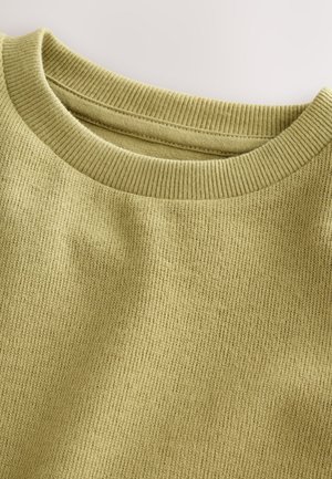 Alyvuogių žalios spalvos megztinis su ribotu apvaliu iškirpimu ir tekstūruotu mezgimo raštu. Audinys atrodo minkštas ir šiek tiek tamprus.