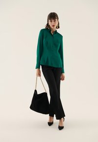 Camicia verde in raso con bottoni, pantaloni neri svasati e borsa in suede nera con tracolla a catena dorata. Modella con tacchi neri a punta.
