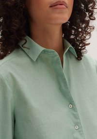 Ljusgrön, kragskjorta i mjukt tyg, med knappstängning fram och små runda knappar samt en avslappnad passform.