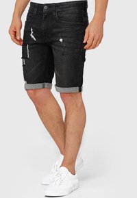 Pantaloni scurți din denim negru cu tivuri întoarse, detalii uzate și buzunare laterale. Purtați cu adidași albi.