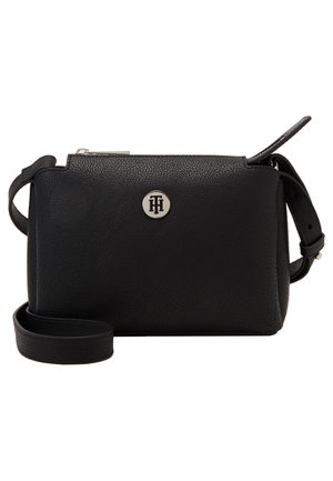 Black textured leather crossbody bag with adjustable strap and silver circular logo emblem on front center.