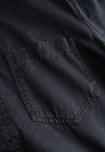 Mustast kangast lähedalt vaadatav tasku, millel on nähtav topeltõmblus riietel.