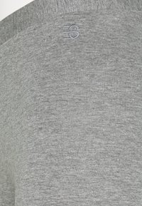 Grått textil med en mjuk, slät textur och ett subtilt, något melerat mönster. En liten broderad logotyp syns i det övre området.