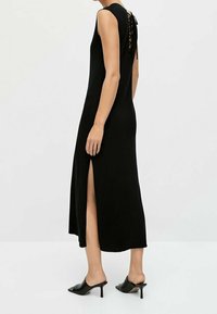 Vestito nero senza maniche con schiena con lacci, spacco laterale, lunghezza al ginocchio, realizzato in tessuto liscio. Abbinato a mule neri.