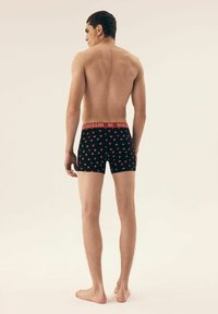 Czarne bokserki w czerwone wzory serc, z czerwonym paskiem z napisem "HENDERSON", widoczne od tyłu. Gładki materiał, dopasowany krój.