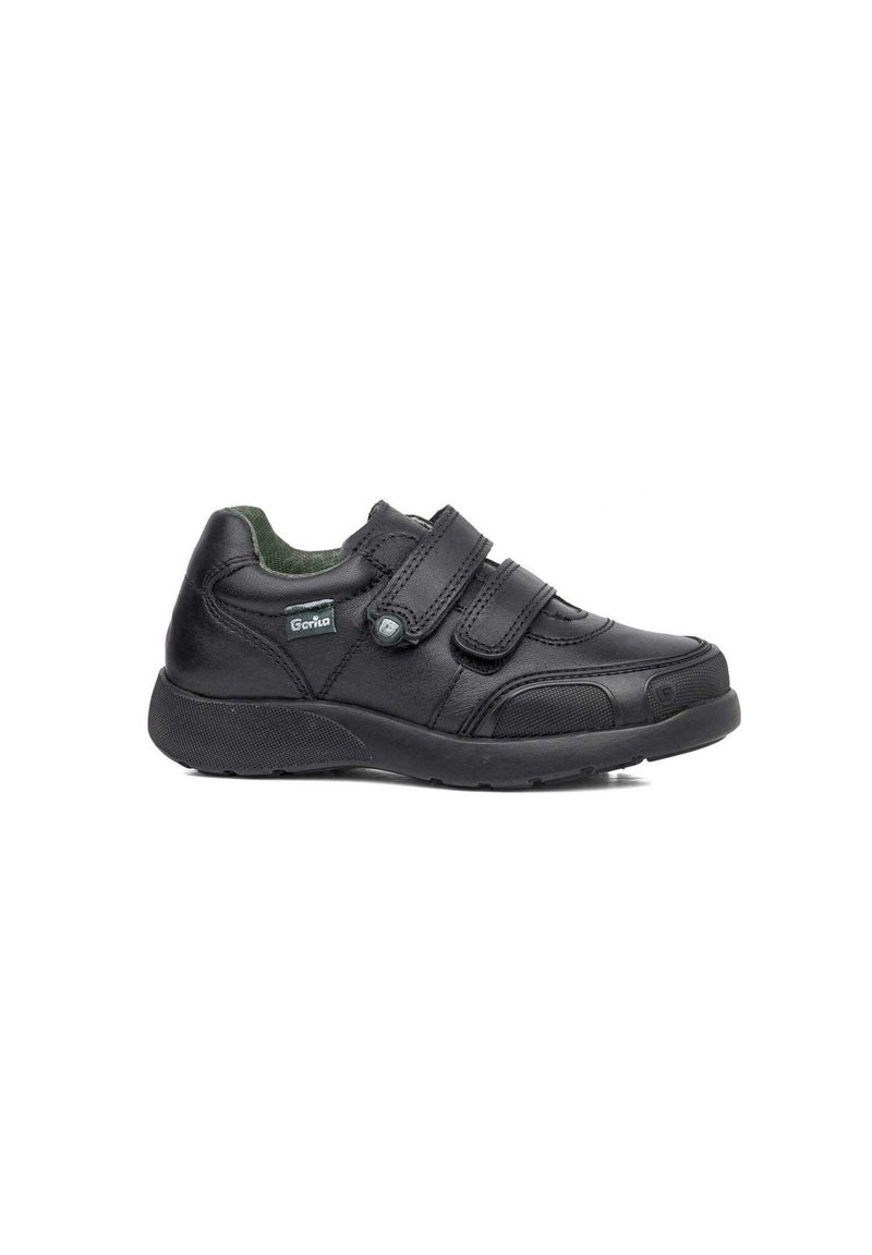 Zapato de cuero negro con dos correas de velcro, punta redondeada, suela texturizada y un forro interior verde. Presenta un parche con el logo en el lateral.