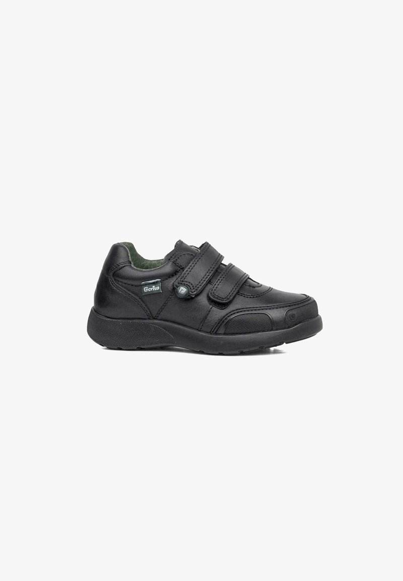 Zapato de cuero negro con dos correas de velcro, punta redondeada, suela texturizada y un forro interior verde. Presenta un parche con el logo en el lateral.