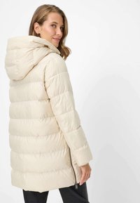 Lyse beige dunjakke med hætte, vandret quiltet mønster, lynlås foran og sidelommer. Blød tekstur og afslappet pasform.