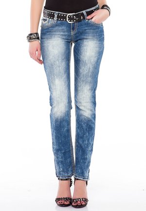 Schmale blaue Denim-Jeans mit Ausbleichungen und abgetragenen Bereichen, ausgestattet mit einem silbernen Kettenakzent entlang der Nähte und einem schwarzen, mit Nieten besetzten Gürtel.
