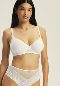 Biały stanik z usztywnianymi miseczkami, koronkowymi akcentami i regulowanymi ramiączkami. Majtki w wysokim stanie w tym samym stylu, z przezroczystymi panelami i koronkowymi detalami.