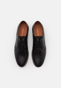 Chaussures en cuir noir avec un bout arrondi, des lacets plats et une finition lisse. L'intérieur est doté d'une semelle intérieure marron avec le logo "ANNA FIELD" embossé.
