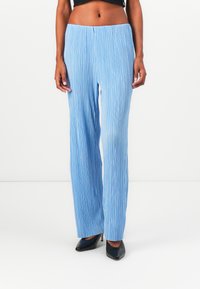 Pantalons larges plissés bleu clair avec une surface texturée, dotés d'une taille haute et d'une coupe décontractée, associés à des escarpins noirs à bout pointu.