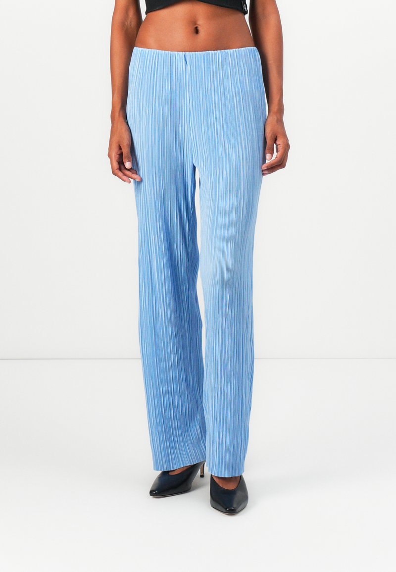 Pantalons larges plissés bleu clair avec une surface texturée, dotés d'une taille haute et d'une coupe décontractée, associés à des escarpins noirs à bout pointu.