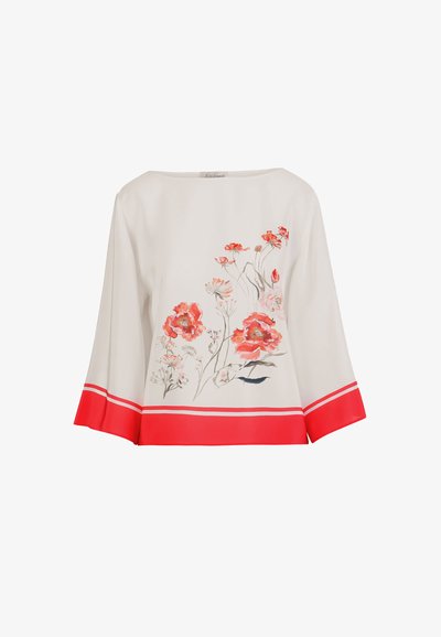 Blouse blanche à manches longues avec imprimé floral rouge sur le devant et larges poignets rouges avec des rayures blanches aux manches et à l'ourlet.