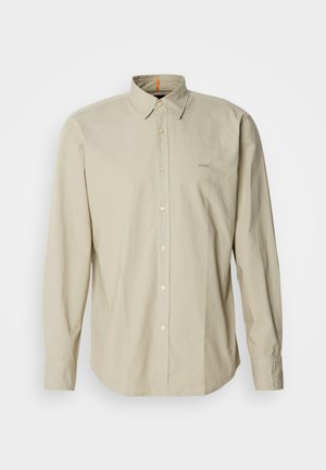 Beige long-sleeve button-up shirt with a structured collar, featuring a patch pocket and subtle logo embroidery on the chest. Smooth, lightweight fabric.