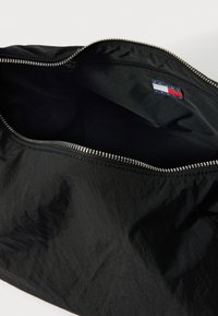 Fekete nejlon táska zipzáras záródással. A belseje fekete szövettel bélelt. A cipzár közelében egy kis, kék, fehér és piros címke található.