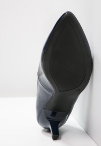 Chaussure à talon haut en cuir verni bleu marine avec bout pointu, talon aiguille fin et semelle en caoutchouc noir texturée.