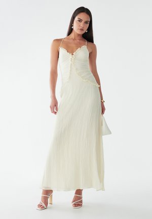 Cremfarbendes Maxikleid mit Rüschensaum, strukturiertem Stoff, dünnen Schulterträgern und einem taillierten Oberteil, das in eine A-Linie übergeht.