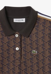 Braun und marineblau gemustertes Poloshirt mit Kragen, das ein geometrisches Design aufweist, weiße Knöpfe und ein grünes Lacoste-Logo.