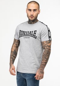 Grey cotton t-shirt featuring bold black "LONSDALE LONDON" text, short sleeves with black and white stripe accents, and a classic fit.