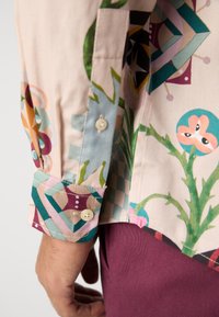 Multicolored long-sleeve shirt featuring a floral and geometric pattern, made of cotton, with a buttoned cuff and textured fabric.