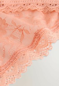 Perzikkleurige kantstof met bloempatronen, gegolfde randen en een delicate, textuurvolle oppervlakte met open wevingen en ingewikkelde stiksels.