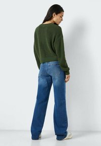 Mørkegrønn strikkegenser med avslappet passform, kombinert med lyseblå vide jeans, sett bakfra mot en nøytral bakgrunn.