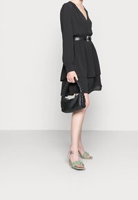 Svart klänning med djup V-ringning, långa ärmar och lager på nederkanten. Bärs med gröna flätade klacksandaler och en svart flätad handväska.