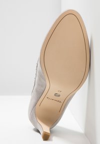 Chaussure à talon haut en daim gris clair avec un bout pointu, présentant une semelle lisse et un détail accent doré sur le talon. Taille 37 indiquée sur la semelle.