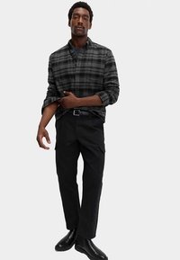 Sort og grå ternet skjorte med knapper og lange ærmer, kombineret med sorte bukser og skinnende sorte støvler. Enkel, ren design samlet set.