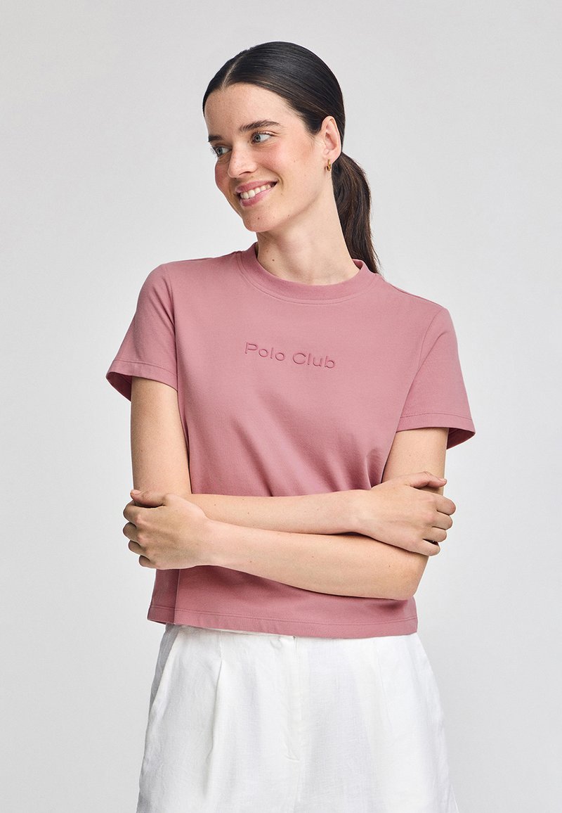 Kort rosa bomull t-shirt med rund halsringning, korta ärmar och präglad "Polo Club"-logotyp på framsidan. Matchad med vita texturerade byxor.