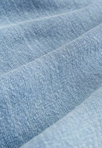 Tissu en denim bleu clair avec un tissage texturé, présentant des lignes diagonales et une sensation douce. Le gros plan met en évidence les fins détails des fibres.